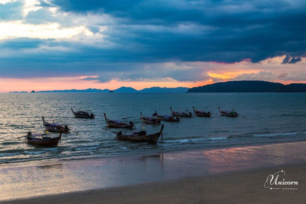 Private Transfer from Phuket to Ao Nang Beach – Fixed Price & Door-to-Door 3 Long-tail boats floating on the calm sea at Ao Nang during sunset